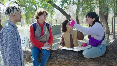 Cheerful Students Sitting on Tree in the Park and Doing Homework