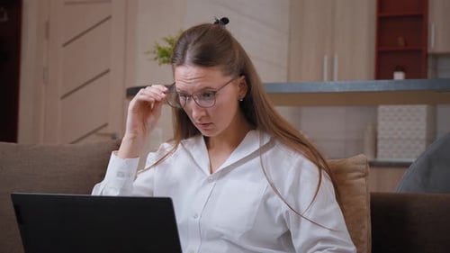 Junge Frau passt die Brille an und schaut verwirrt auf den Laptop-Bildschirm