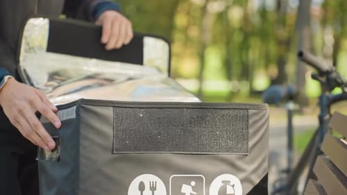 Courier Food Delivery Cyclist asegura el contenedor reutilizable en una bolsa aislante en Park Bicycle Courier