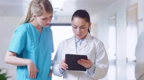 In the Hospital, Busy Doctors Talk, Using Tablet Computer While Standing in the Hallway. New Modern