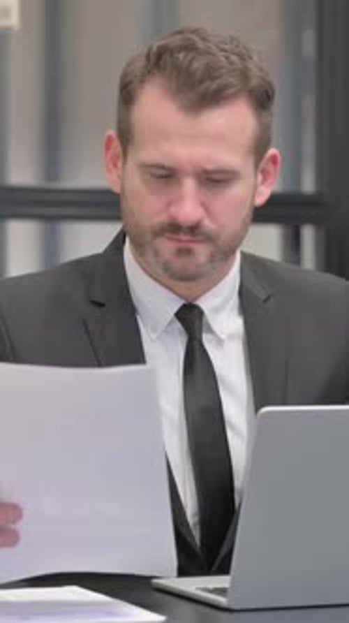 Man Working on Laptop and Reviewing Documents