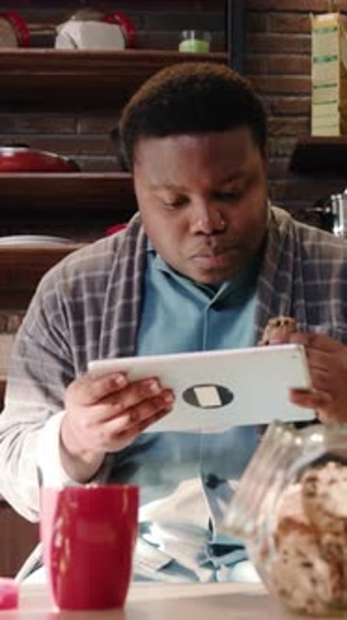 A Relaxed Man is Enjoying a Tasty Snack While He Happily Uses His Tablet in a Cozy Kitchen Space
