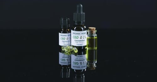 Vídeo em 4K de frascos de óleo de cbd e cápsulas de gel em uma mesa contra um fundo preto de estúdio