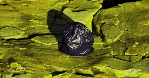 Bolsa de basura negra que descansa sobre una superficie verde rocosa en un entorno natural