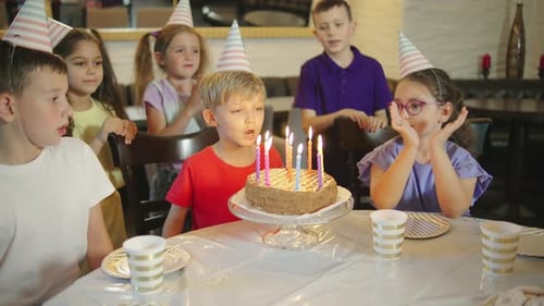 Um aniversariante com um boné festivo apagando as velas de um bolo de aniversário e seus amigos rindo