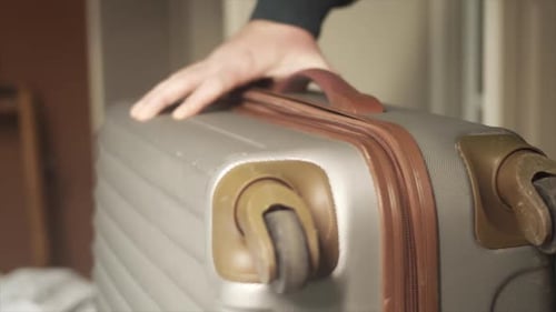 Person zips grey suitcase shut and carries out of frame, Close Up