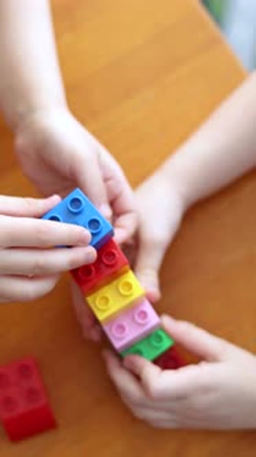 Nahaufnahme von Händen, während zwei Kinder mit einem lustigen Bauset kreative Strukturen bauen