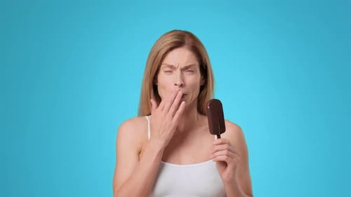 Young Woman Enjoying Chocolate Ice Cream on a Blue Background With a Cheerful Expression