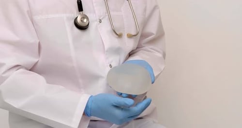 Doctor Examines Breast Implant in Blue Gloves