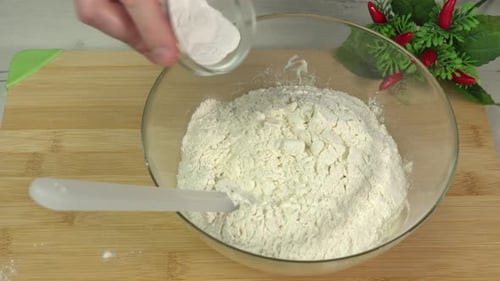Man adding baking powder to flour in a glass bowl for making shortcrust pastry. Cooking pastry
