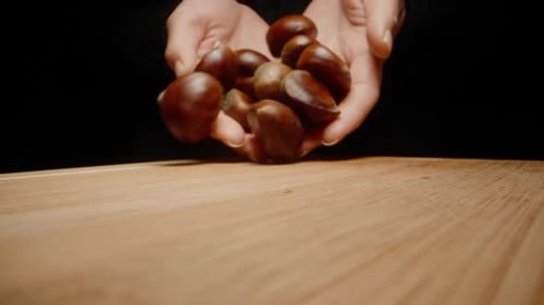 Girl pours a handful of peeled chestnut nuts on a wooden table, on a black background, slow motion