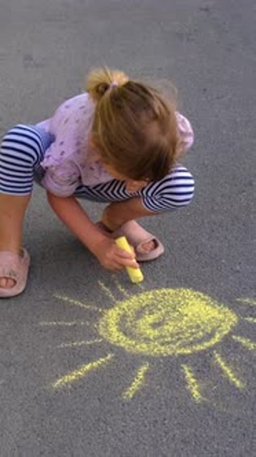 Little Girl Drawing a Sun With Yellow Chalk on Asphalt