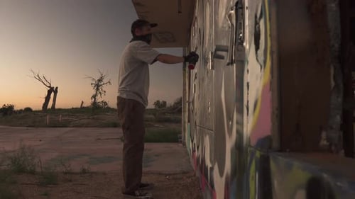 Jovem artista de rua masculino pintando grafite com spray em prédio abandonado