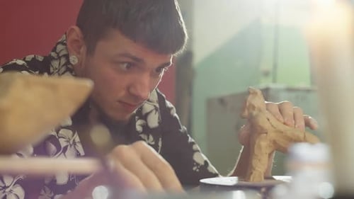 Young Adult Sculpting a Clay Figure at his Workbench