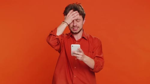 Confused Man Using Cell Phone on Orange Backdrop
