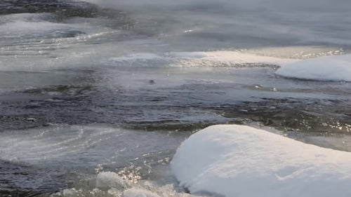 Water flows down an icy river, as ice melts on a sunny winter day.