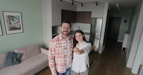 Happy Married Couple Owners of a New Apartment Show the Key Looking at Camera Wife and Husband Hug