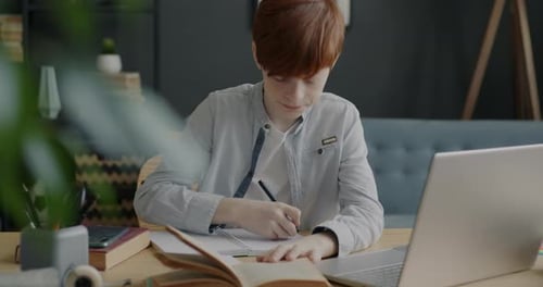 Teen Studying Book at Home Desk with Laptop