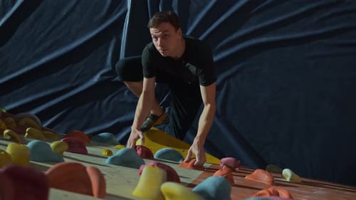 Focused Man Rock Climbing on Indoor Training Wall