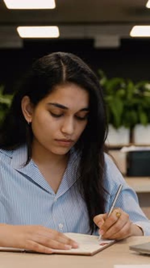 Focused Young Indian Businesswoman Writing in Notebook at Office Desk
