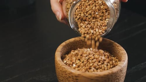 Pouring Buckwheat into Wooden Bowl in Close Up