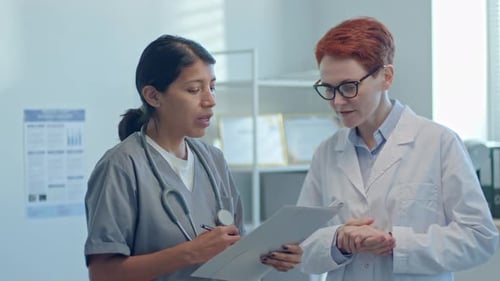 Female Doctor and Nurse Discussing Medical Form in Clinic