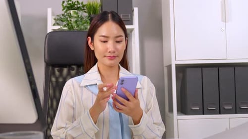 Asian young businesswoman talking on smartphone and working in office.