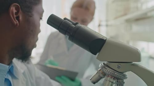 Afroamerikanischer männlicher Mikrobiologe benutzt Mikroskop im Labor