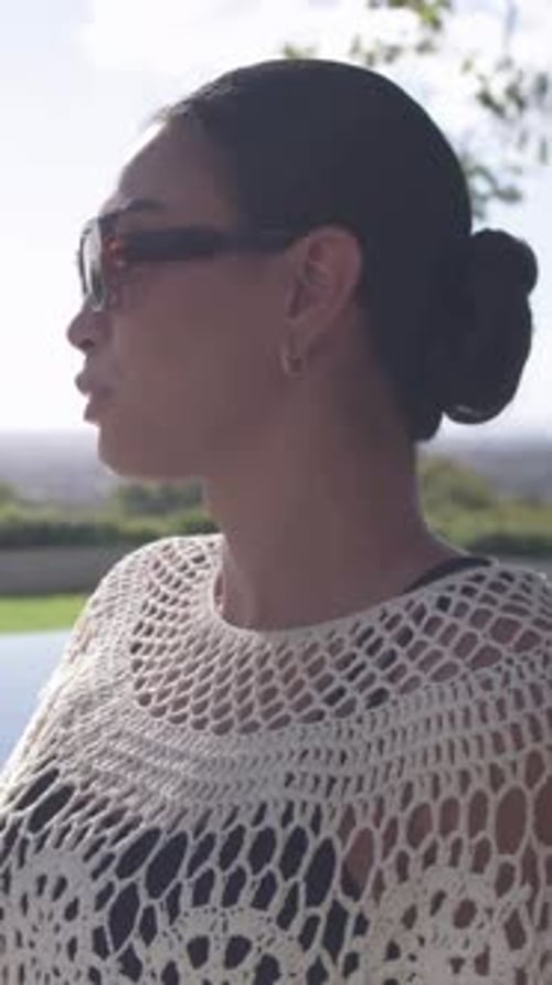 Vertical video: Lifting glass and sipping, woman in crochet turning at pool with tan shades