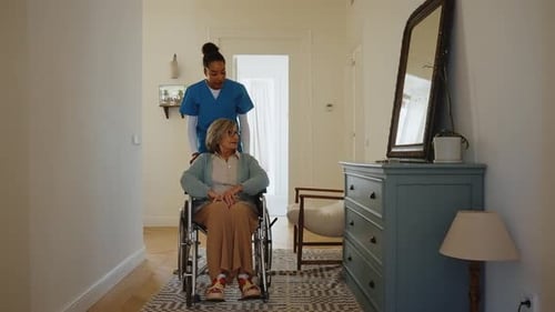 Woman Assists Senior Woman in Wheelchair Indoors