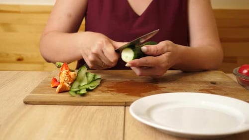 Woman Cutting Fresh Cucumber for Salad at Table