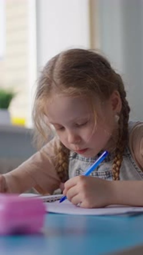 Focused Young Girl with Braided Hair Attentively Writing and Drawing on Paper with a Blue Pen While