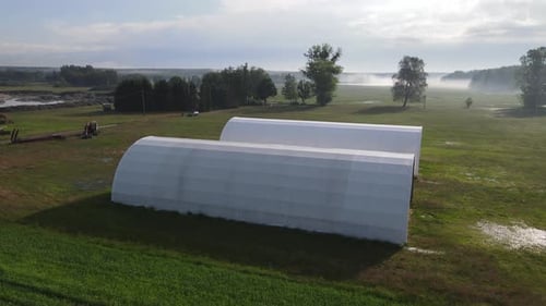 two white arched hall warehouse on farm aerial in sunny morning day