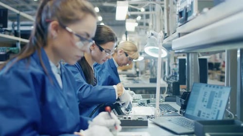 Arbeiterin in einer Elektronikfabrik in blauem Arbeitsmantel und Schutzbrille baut den Laptop M zusammen