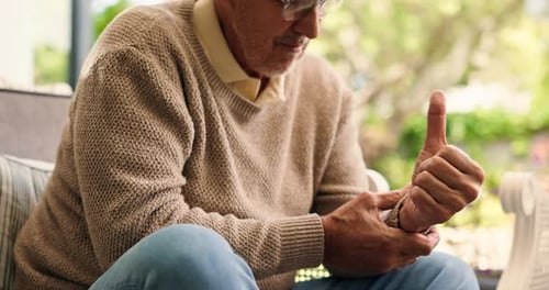 Mature Man Sitting Down Assessing Sore Wrist Outdoors