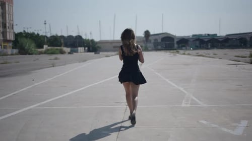 Young Girl Caucasian Woman in Short Black Dress Walking with Her Back in an Industrial Area on the