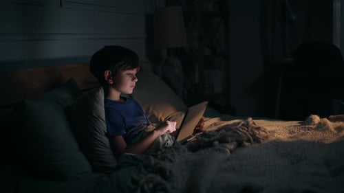Écran lumineux de tablette Addicted Kid Looking dans un appartement sombre, chambre à coucher, appartement