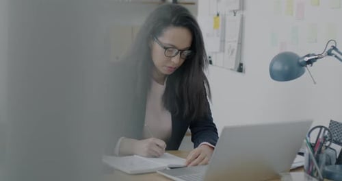 Motivated Businesswoman Working with Laptop and Writing Informaation in Notebook in Office