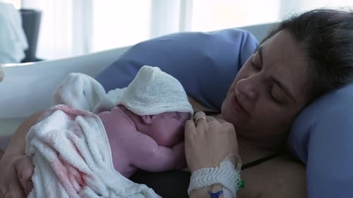 Madre que sostiene al bebé recién nacido justo después de dar a luz, con los primeros segundos de vida del bebé descansando sobre