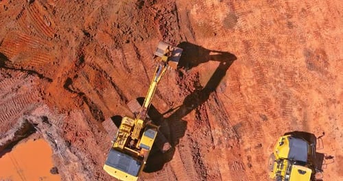 Aerial view of excavator digging deep into reddish brown soil for construction