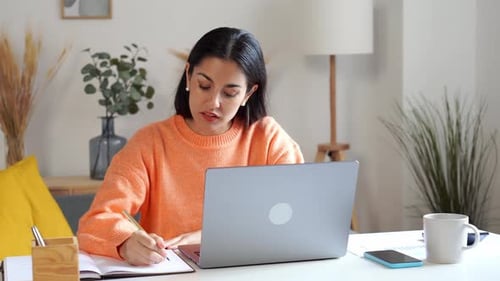 Woman Taking Notes at Desk with Laptop