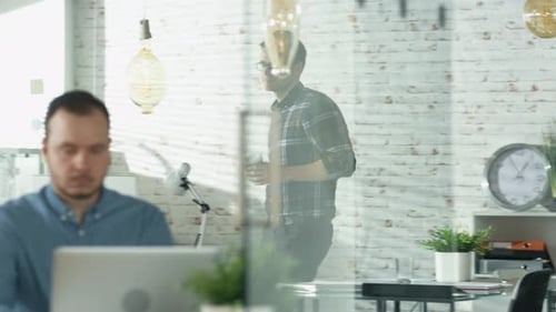 Man Walking into an Office and Sipping Coffee Sits at His Workplace. Starts Working on a Personal C