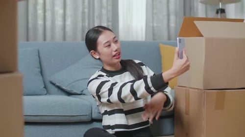Asian Woman With Cardboard Boxes Live Stream By Smartphone After Moving Into A New House