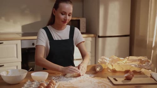 The Concept of Baking Portrait of a Joyful Woman in a Green Apron Kneading Dough in the Kitchen