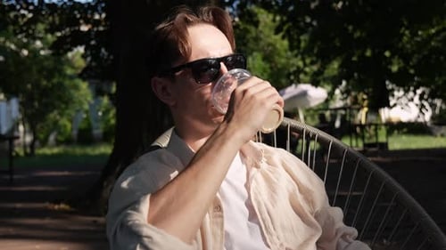 A Young Guy with Glasses Drinking Iced Coffee on a Summer Terrace
