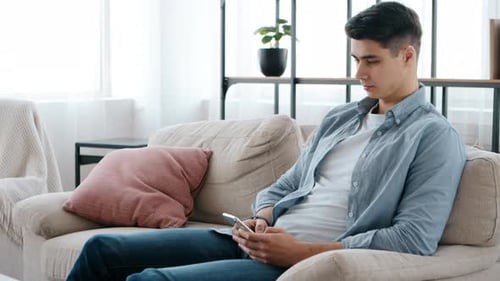Young Adult Using Smartphone Relaxing on Couch Indoors