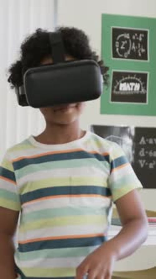 Reaching youth wearing black VR headset tapping, rotating controls at desk striped tee math poster