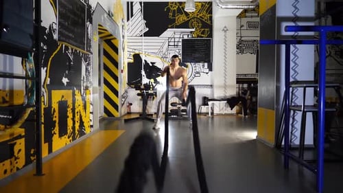Strong Sporty Man Training with Battle Ropes in Sport Club Young Muscular Sportsman Exercising at