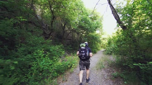 A man with a backpack on his shoulders is climbing up the path against