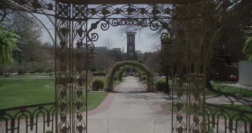 A medium shot through an ornate gazebo towards a path lined with arches and a tall, narrow tower in